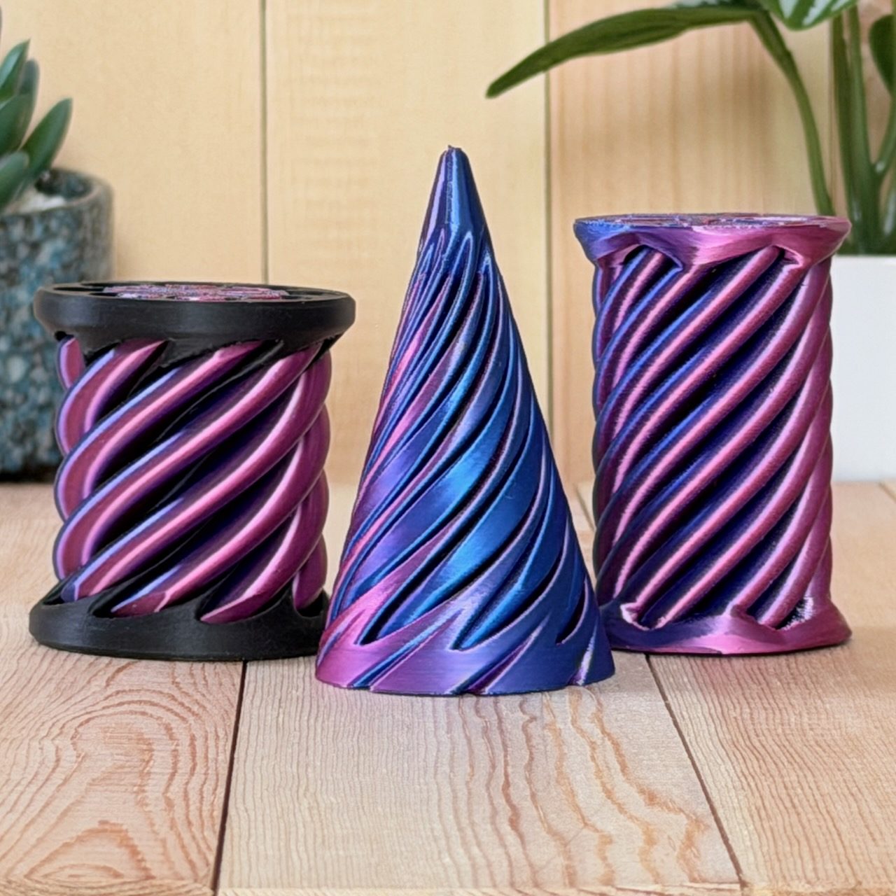 Three spiral fidget toys in magenta, blue and purple silk finish on a wood surface