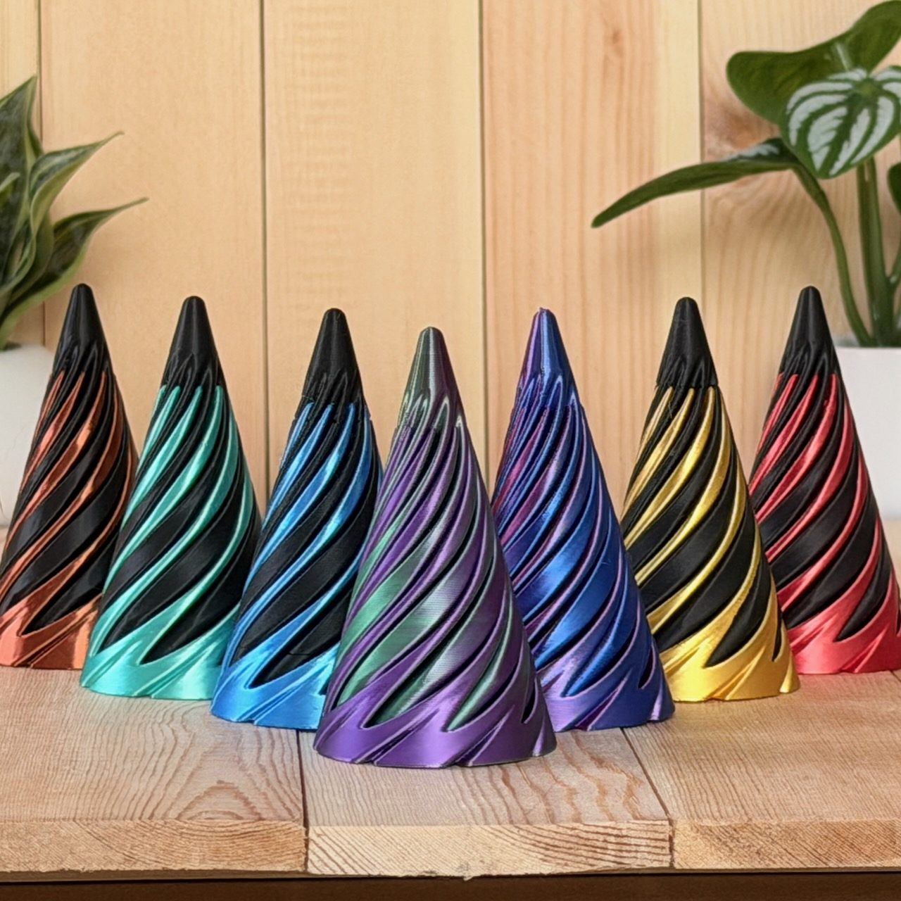 Lineup of twisted spiral fidget cones in teal, purple, blue, magenta, gold and red silk finishes on a wood surface